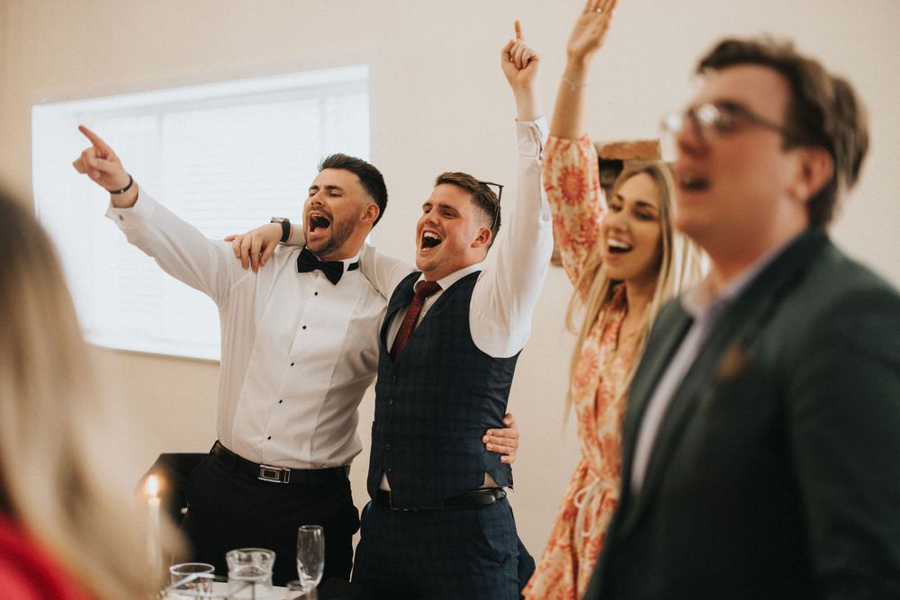 A group celebrates joyfully with raised arms at an indoor formal event, creating an energetic atmosphere.