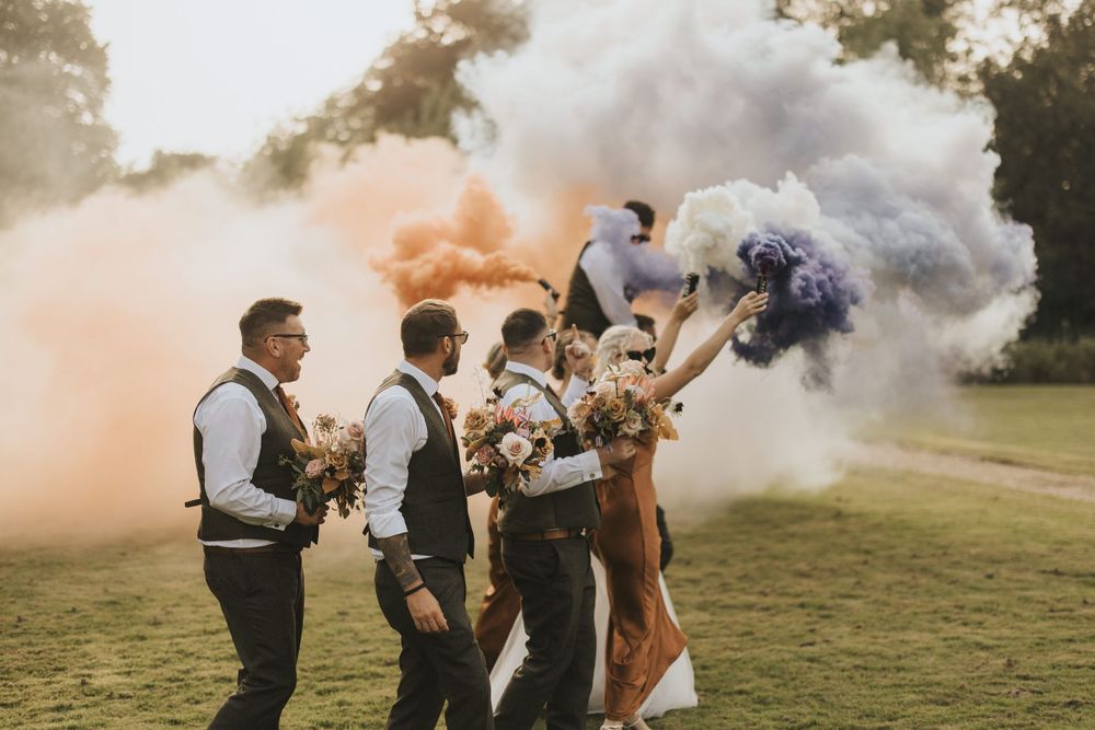 A group of people surrounded by colorful smoke during an outdoor celebration event in a grassy field.
