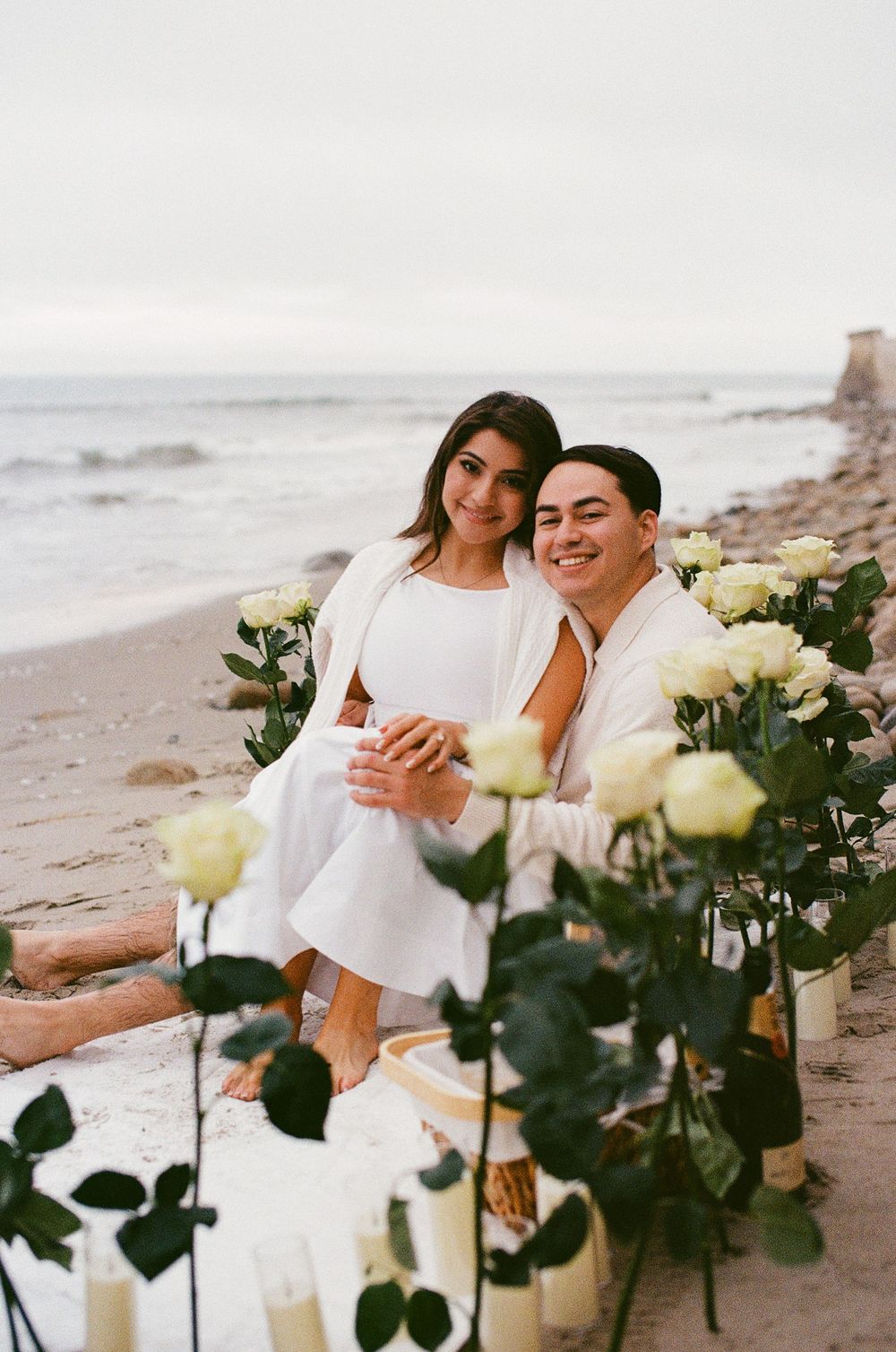 Film photo of couple sitting on blanket, enjoying champagne.