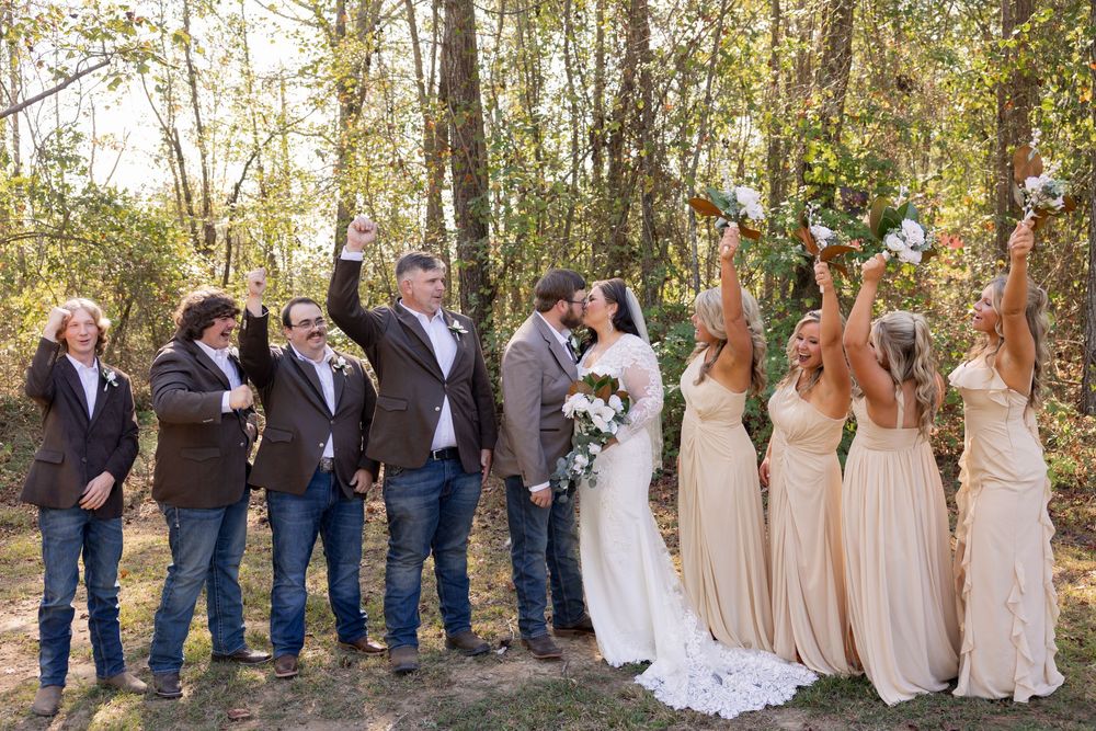 Wedding party lined up outdoors as bridesmaids in beige dresses pose with groomsmen in navy suits.