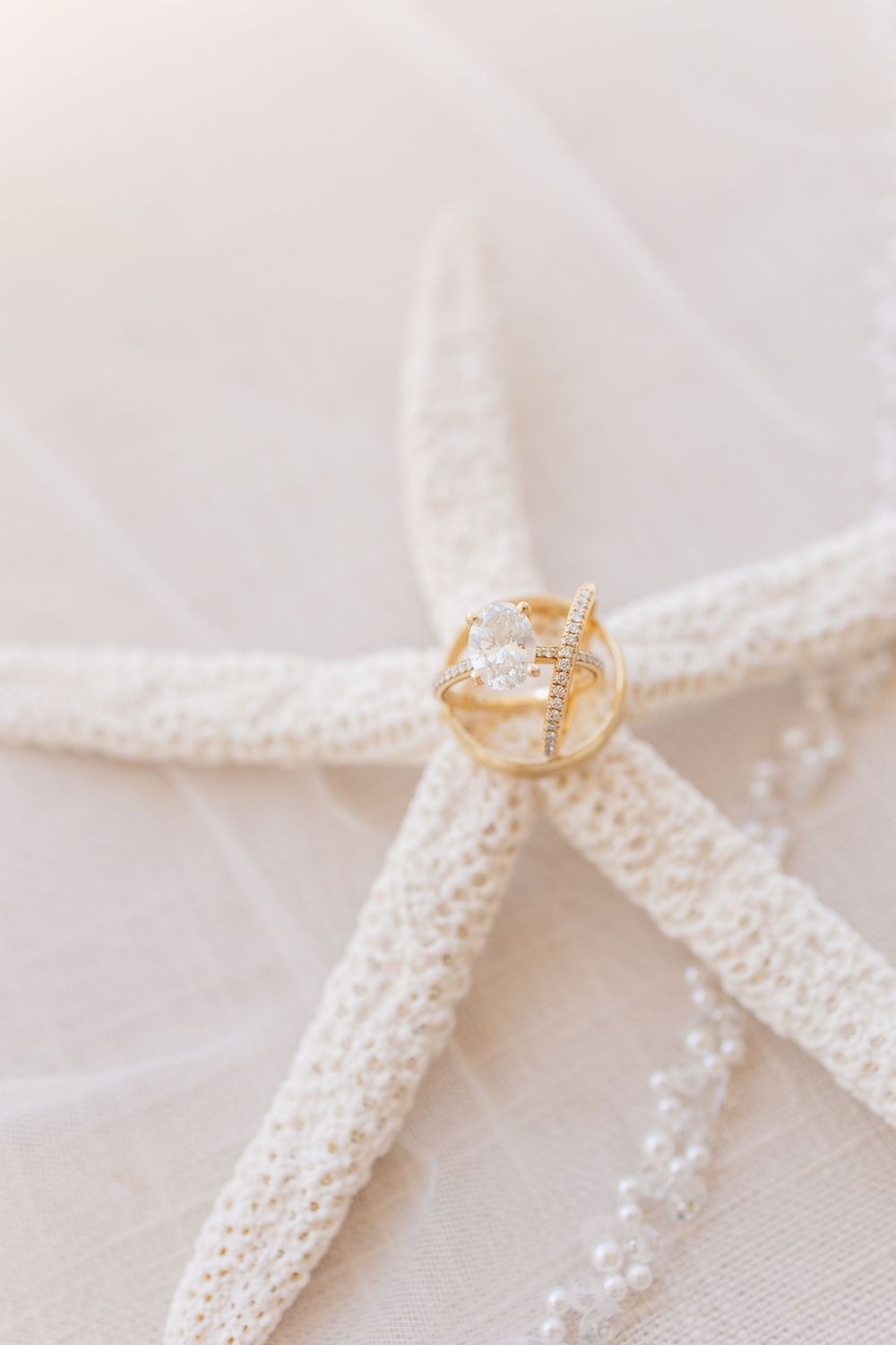 Gold engagement ring with diamonds displayed elegantly on a white starfish against a light fabric backdrop.