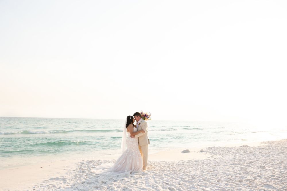 A couple shares a tender embrace on a pristine white sandy beach with turquoise waters in the background.