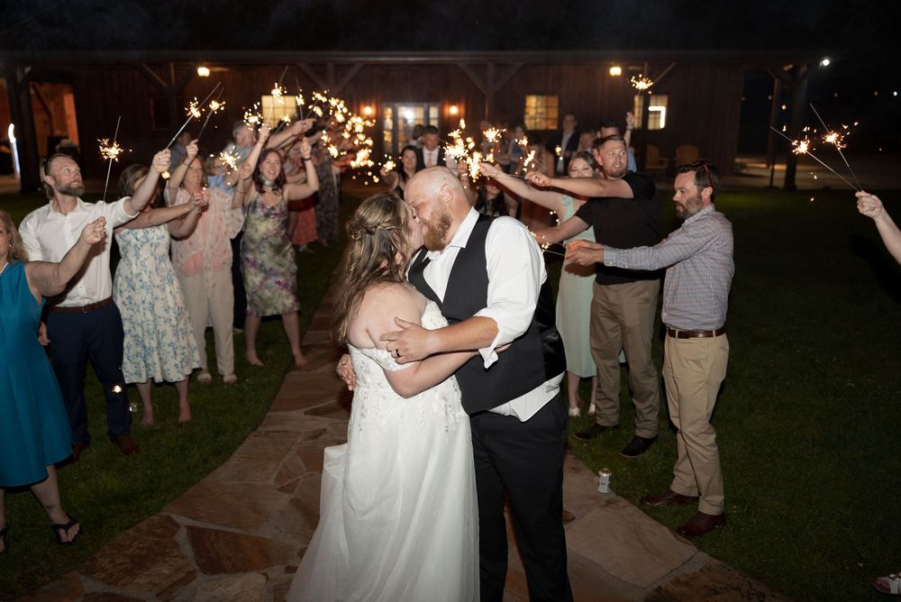 A couple shares their first dance at a nighttime wedding reception while guests cheer with sparklers on the patio.