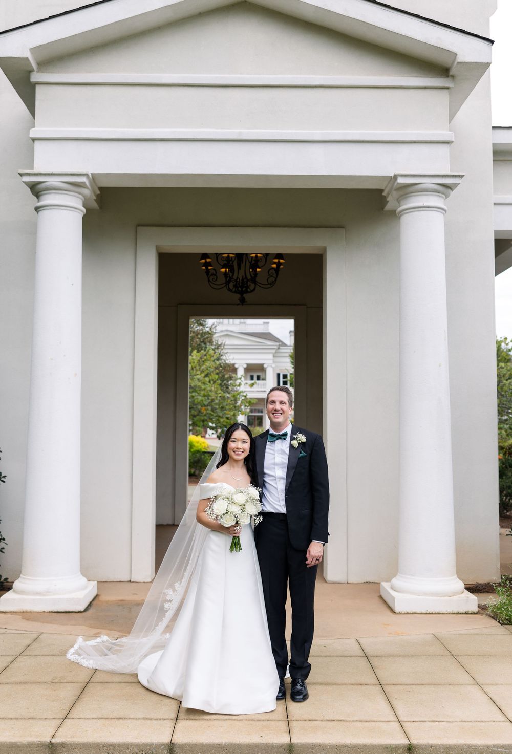 A wedding couple poses under elegant white columns outside a building entrance with classic architecture.