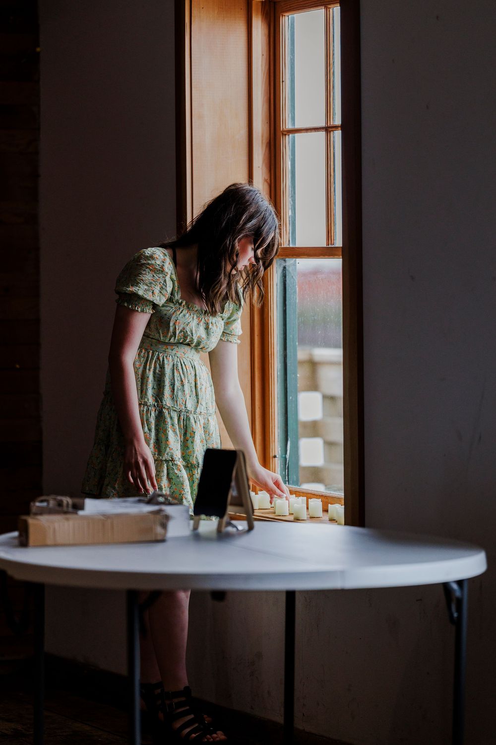 A person in a green dress works on documents at a round table near a sunny window.