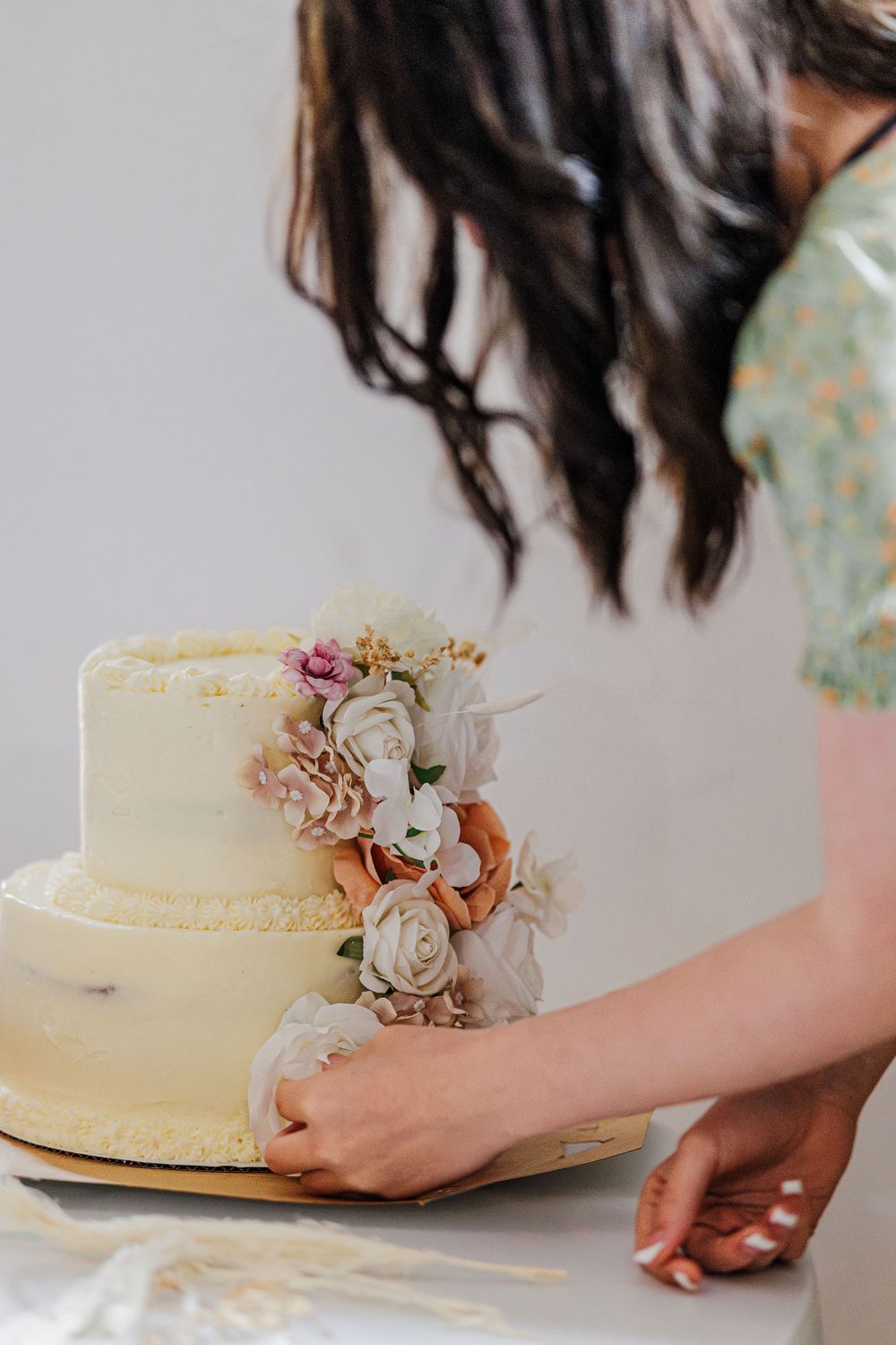 A wedding cake with delicate white floral decorations being carefully positioned on a table.