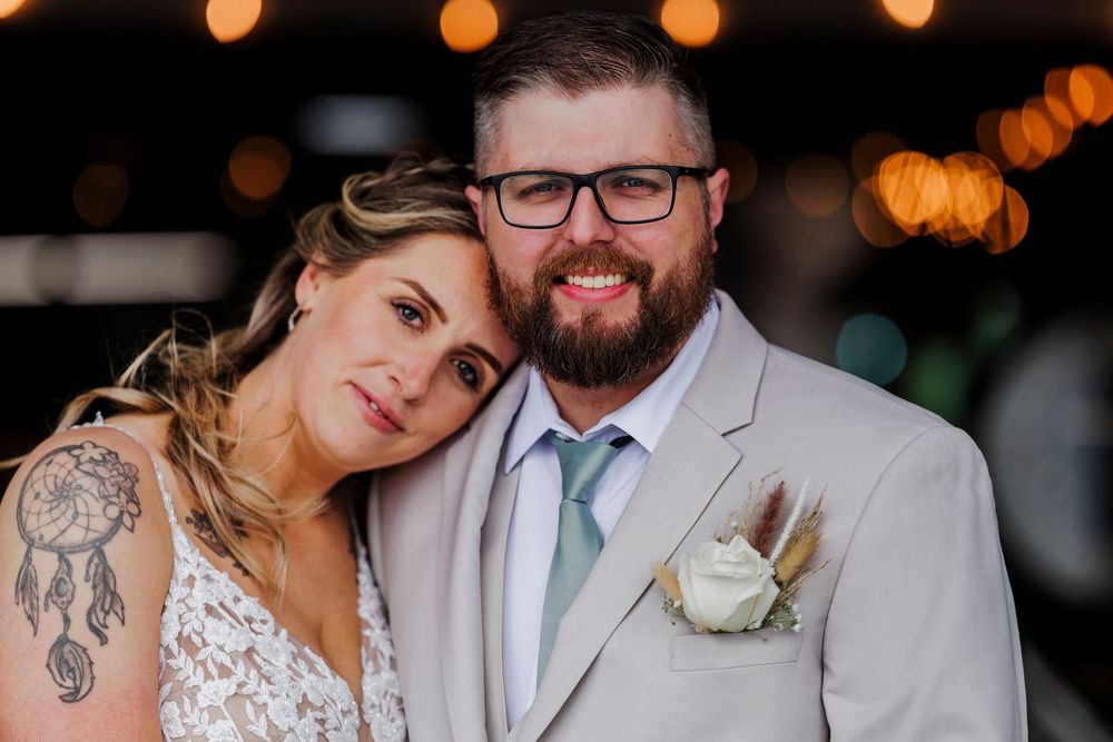 A couple in wedding attire posing together at their reception with soft bokeh lights in the background.