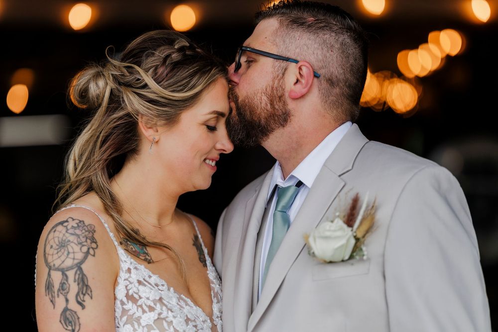 Intimate wedding moment captured under soft glowing lights with mint tie and white boutonniere details.