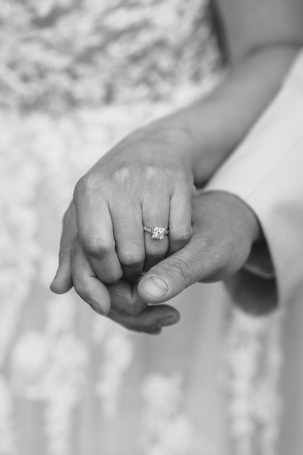 Close-up of hands clasped together showcasing an elegant engagement ring.