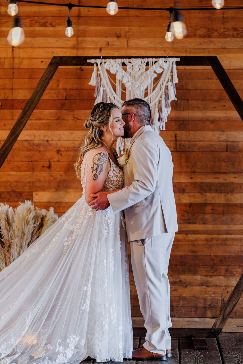 A romantic wedding scene in a rustic wooden barn with glowing string lights overhead.