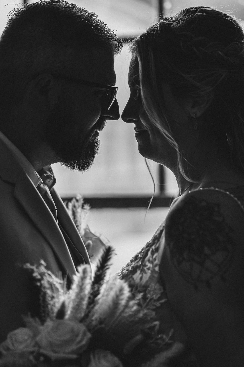 Intimate black and white silhouette portrait with pampas grass accents in soft lighting.