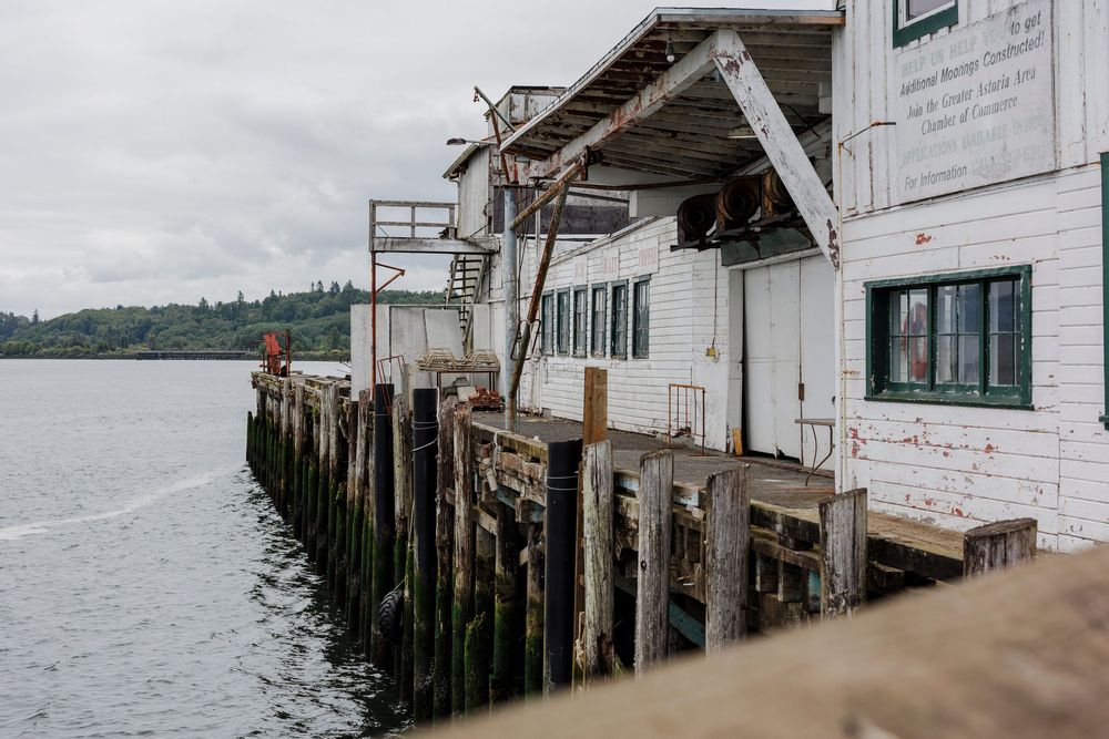Weathered wooden pier structure extends over calm water on cloudy day.