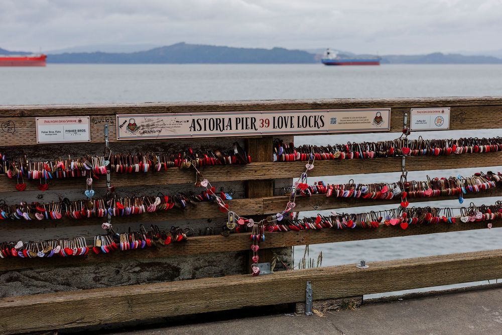 Long row of red and pink love locks attached to a wooden railing with the San Francisco Bay in the background.
