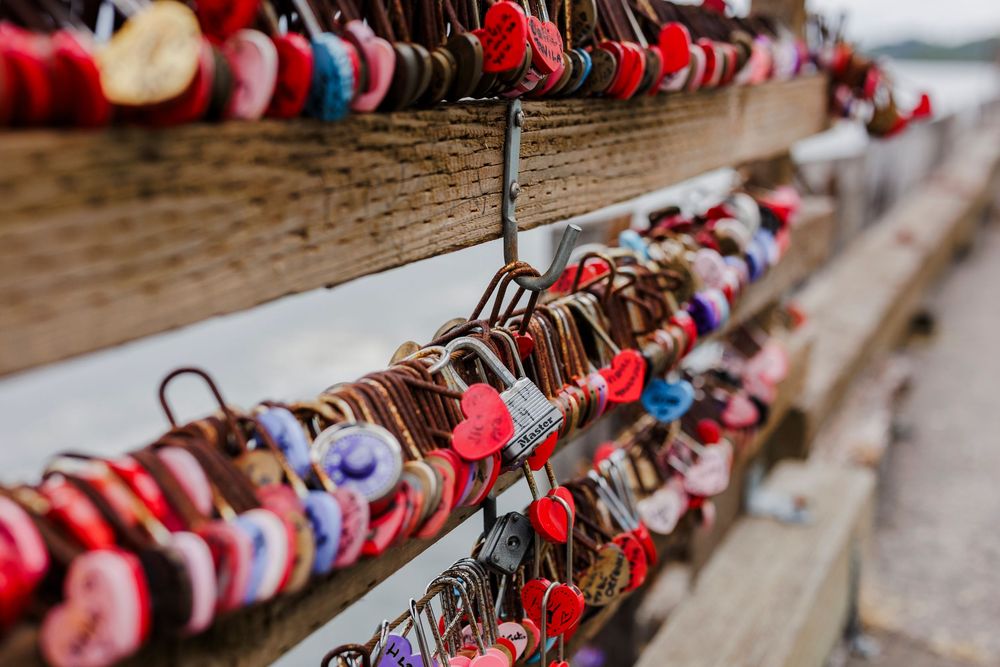 Colorful love locks attached to a wooden railing overlooking the water on a cloudy day.