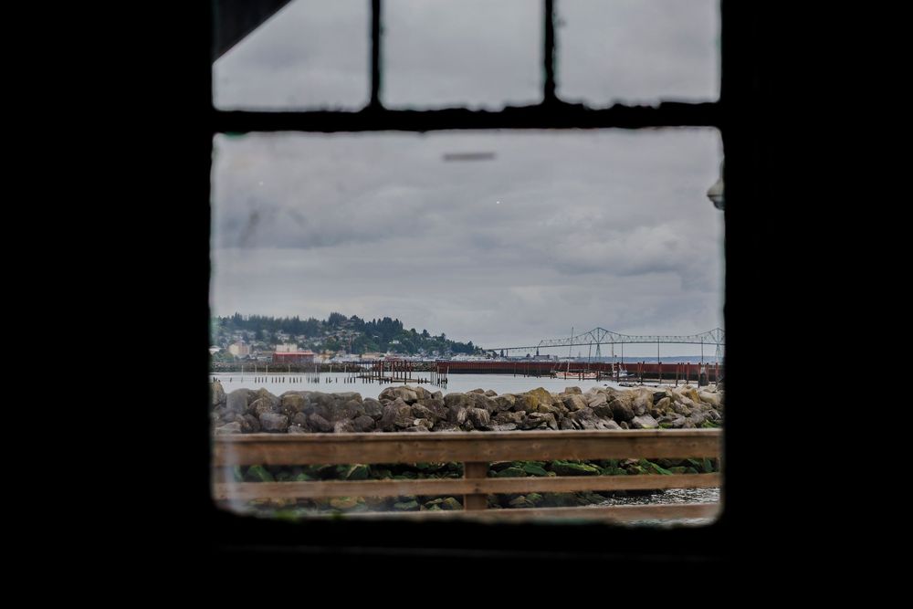 View through a window frame of an industrial waterfront with docked boats and cloudy skies.