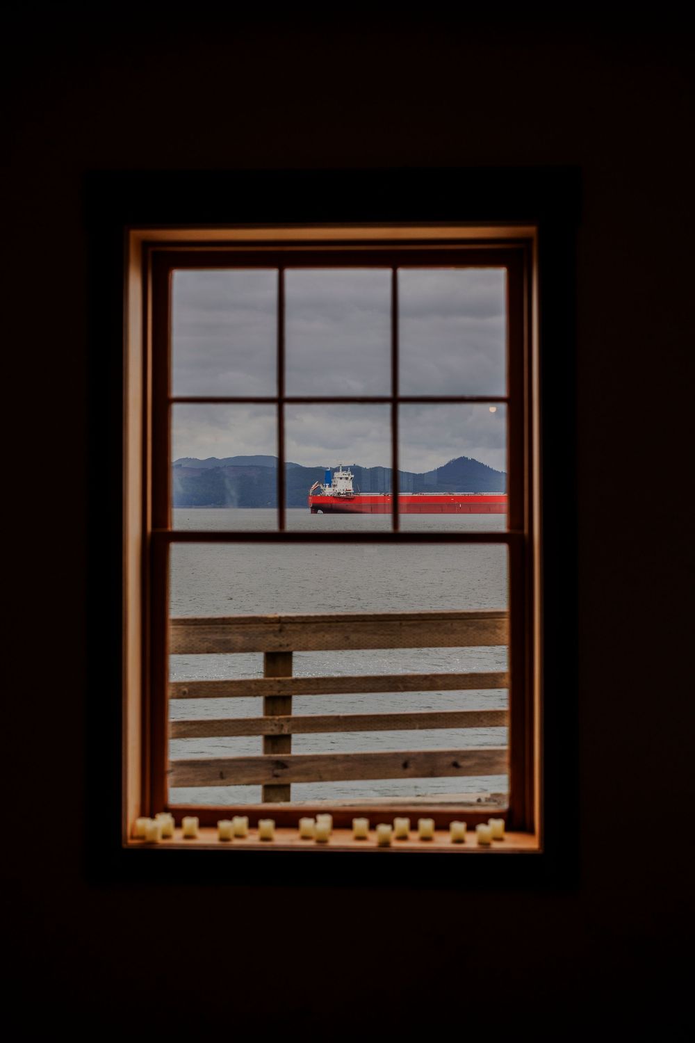 View through a window frame showing a red barn against distant mountains and cloudy sky.