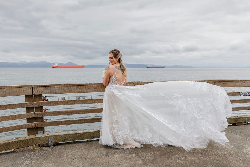 Flowing white wedding dress billowing in the wind against a cloudy coastal landscape.