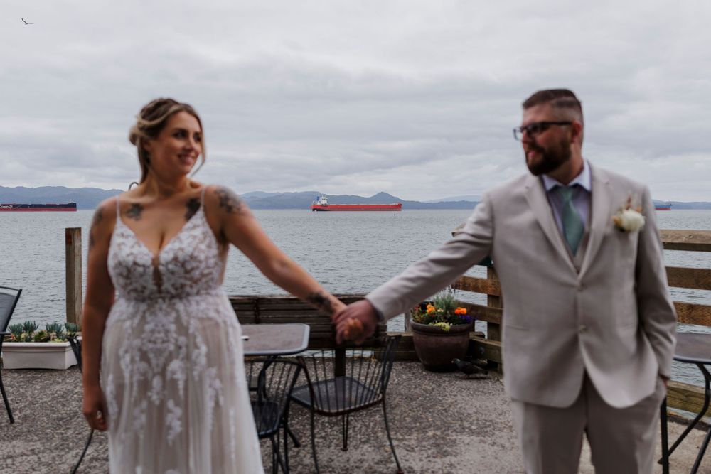 Couple in wedding attire sharing a moment on a waterfront deck with mountain views.