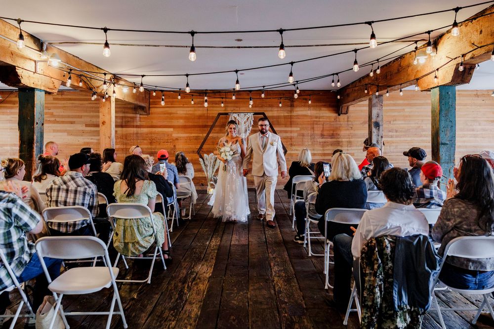 String lights illuminate a rustic barn reception venue with wooden tables and chairs set for a wedding celebration.