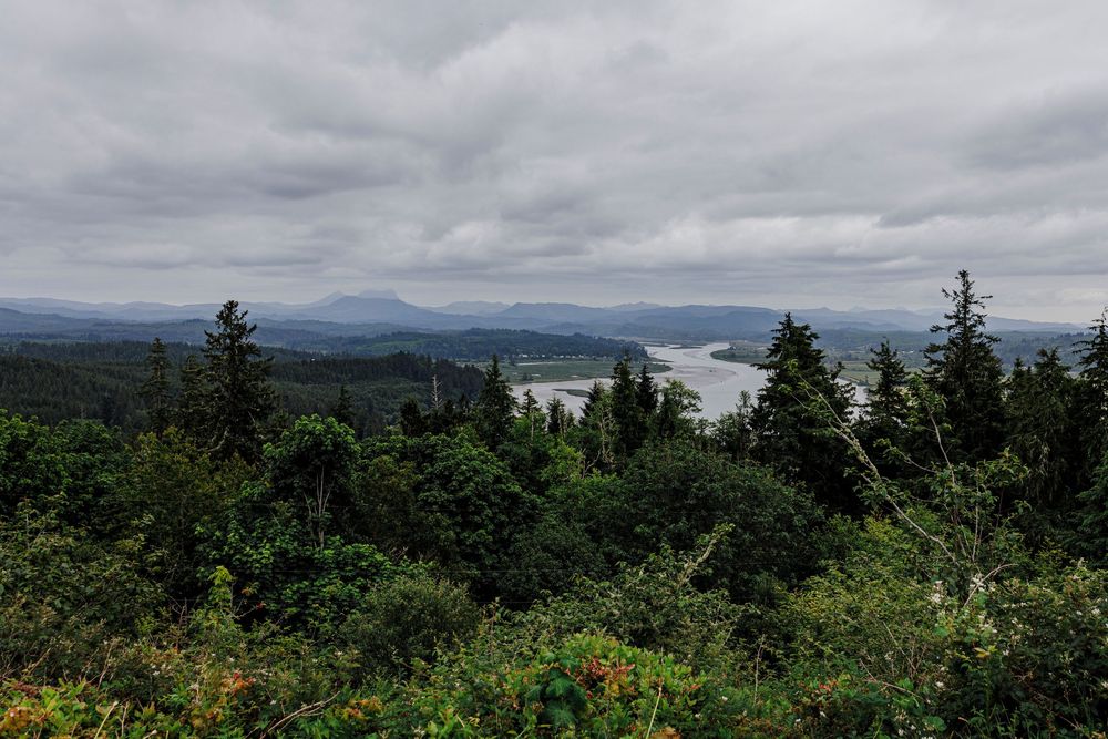 Moody landscape view of mountain forests and water under overcast Pacific Northwest skies.