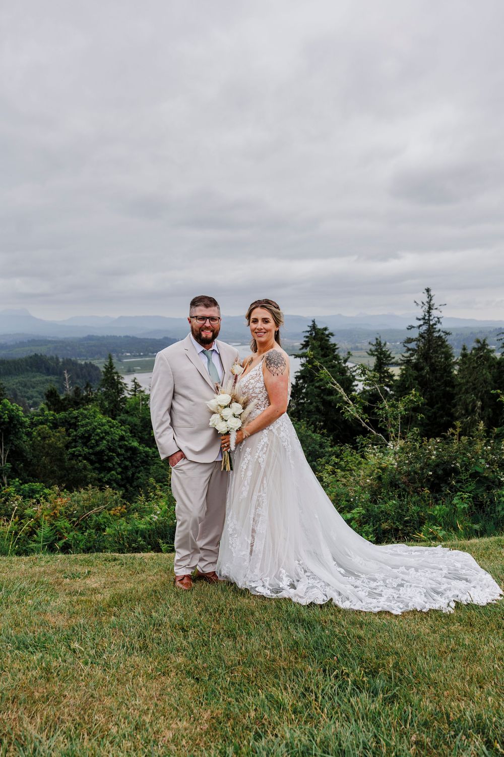 A romantic wedding photo showing scenic mountain views with evergreen trees and cloudy skies in the background.