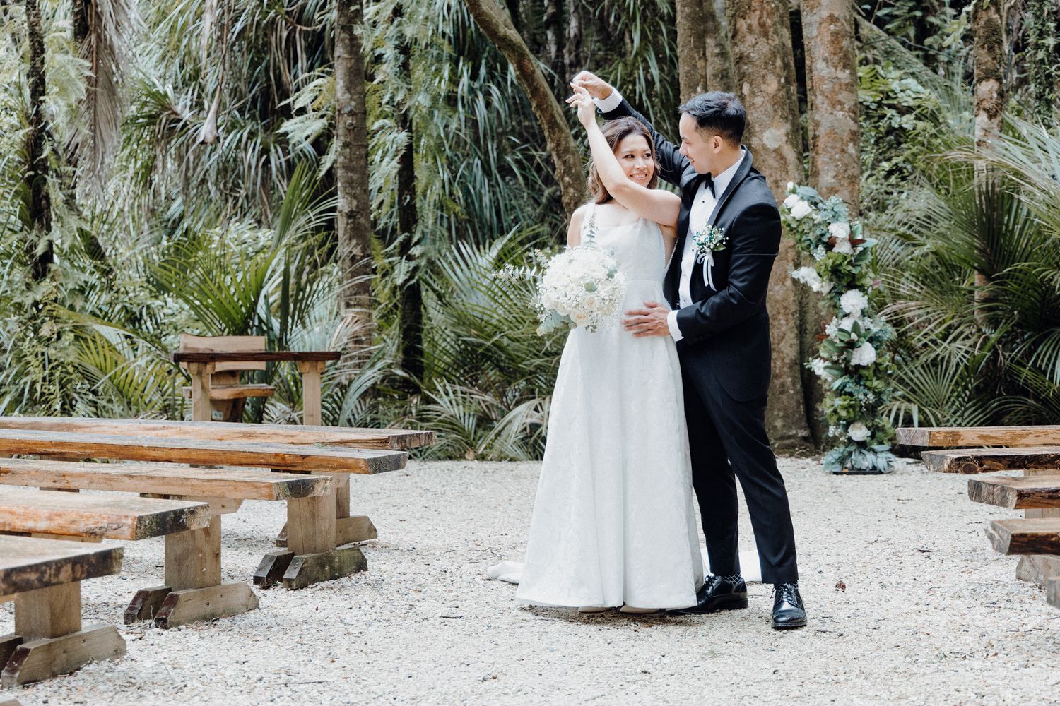 A couple shares an intimate moment in a lush garden venue captured by Apertured Media Auckland Wedding Photographer.