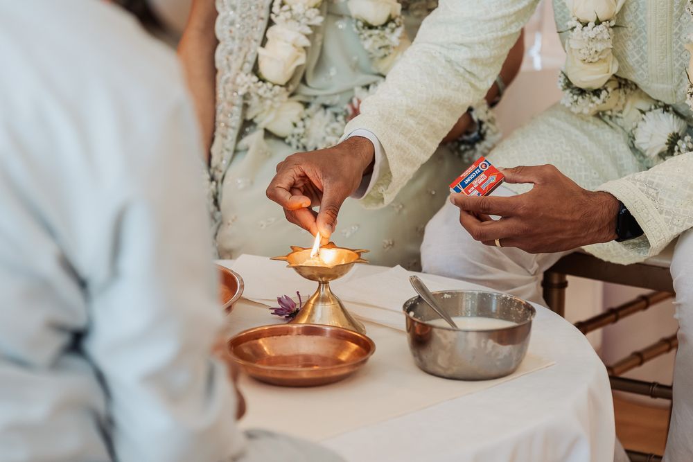 Hands perform a traditional ceremony ritual with small copper bowls and candles on a white tablecloth.