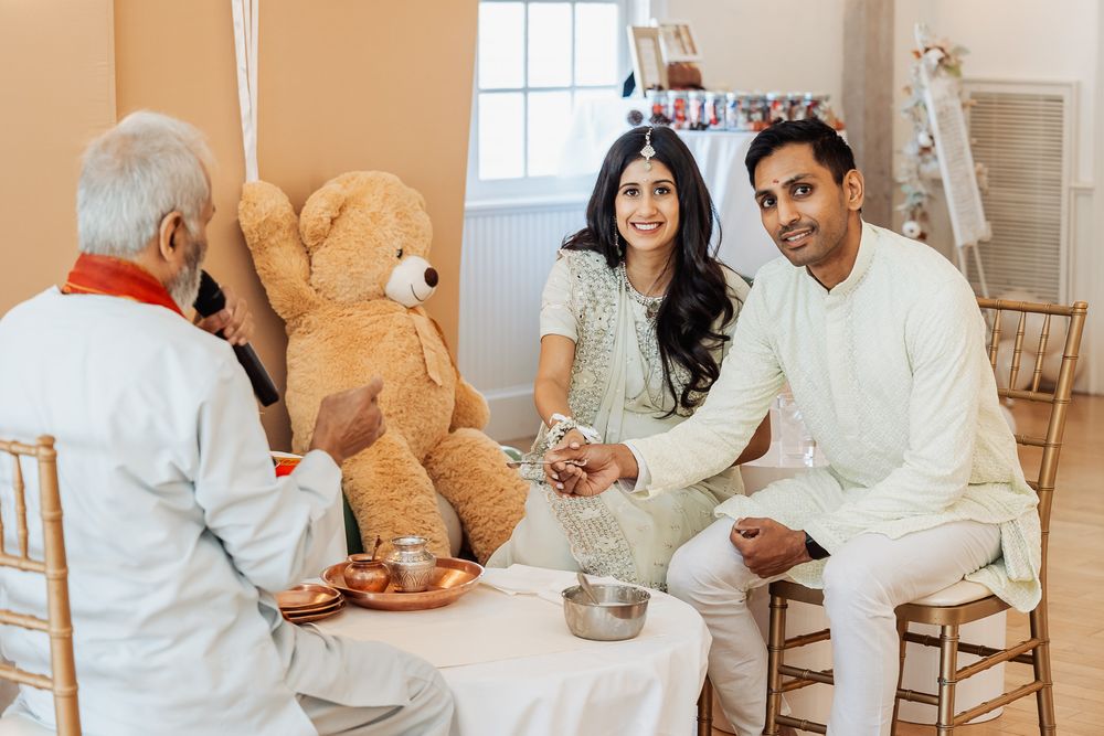 A couple sits at a table with an elder during a traditional ceremony with a teddy bear nearby.