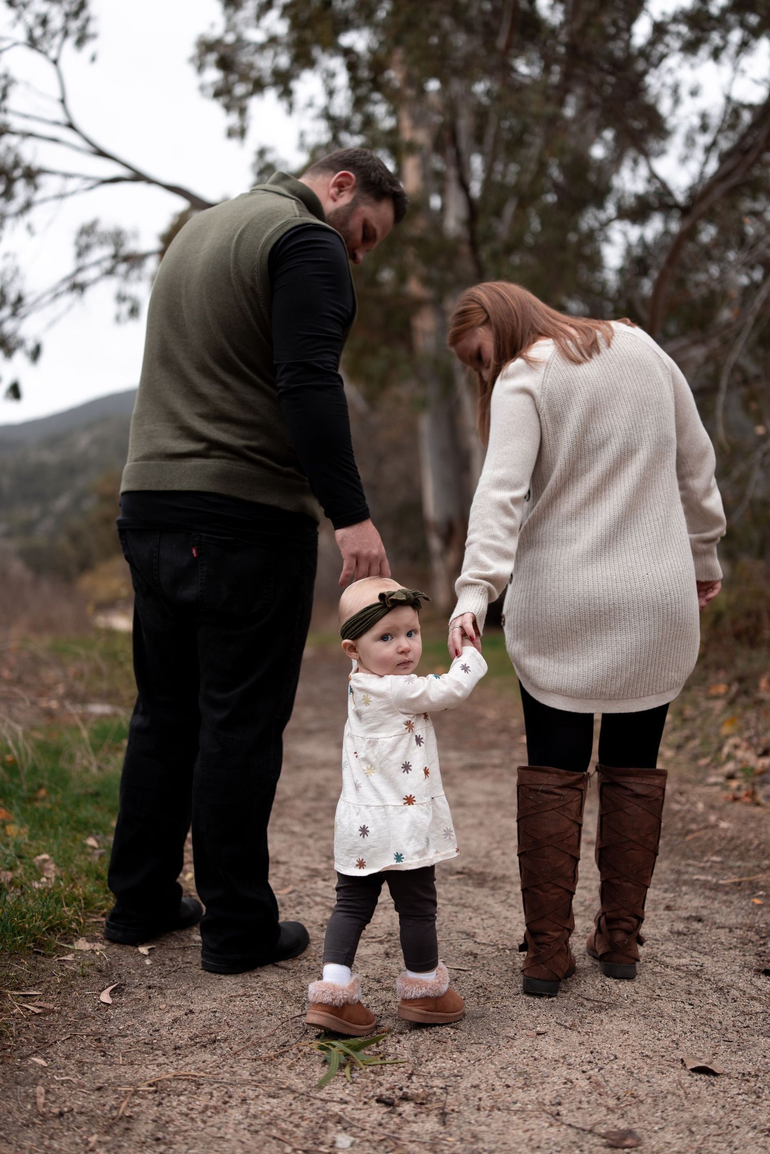 Family enjoying a walk together on a nature trail during autumn, with parents holding hands with small child.