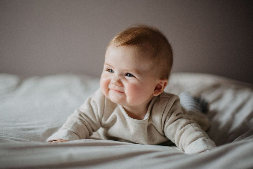 Baby in cream sweater smiling while lying on bed.