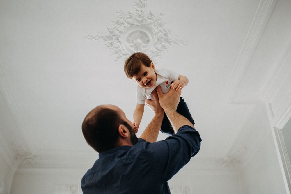 A tender moment captured as a parent lifts a small child up towards an ornate white ceiling.