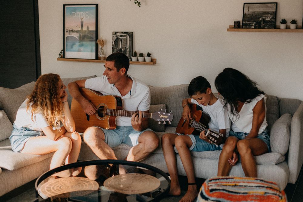 Friends playing acoustic guitars together in cozy living room setting.