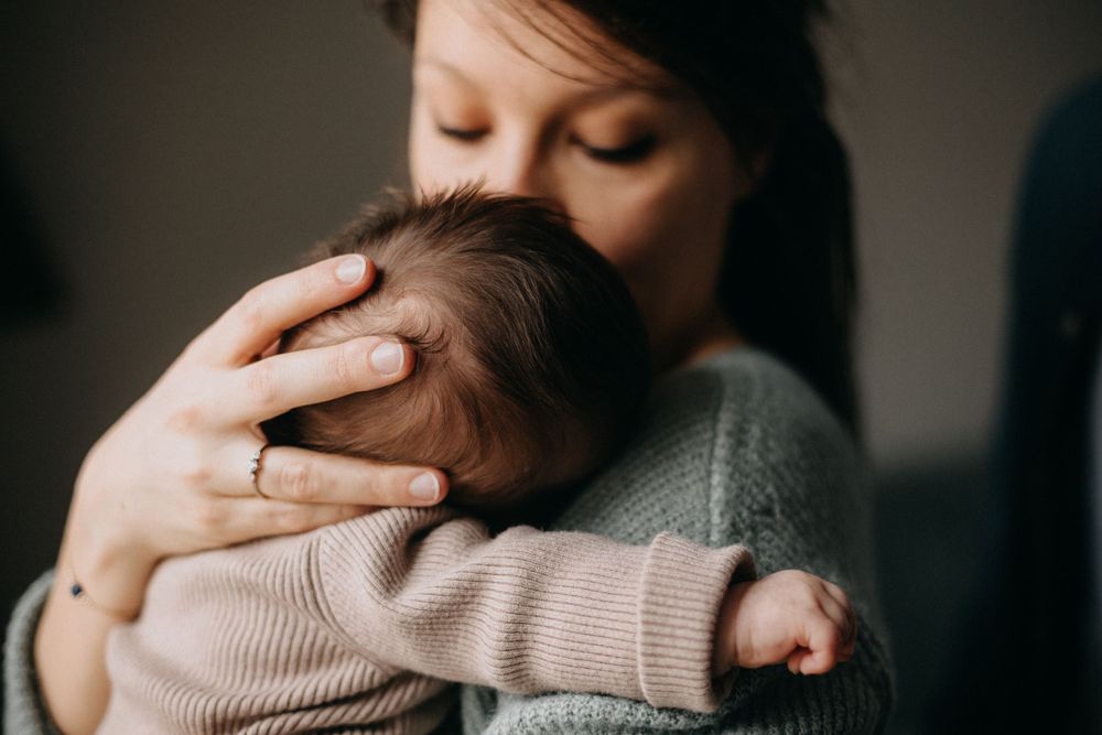 A gentle embrace between parent and baby in soft, natural light.