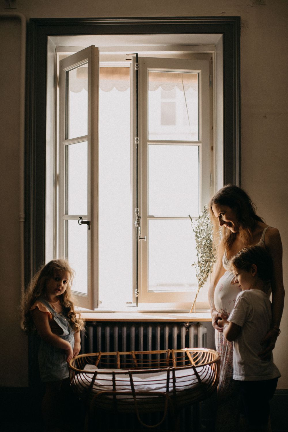 Silhouette of family members standing by window with bassinet in foreground.