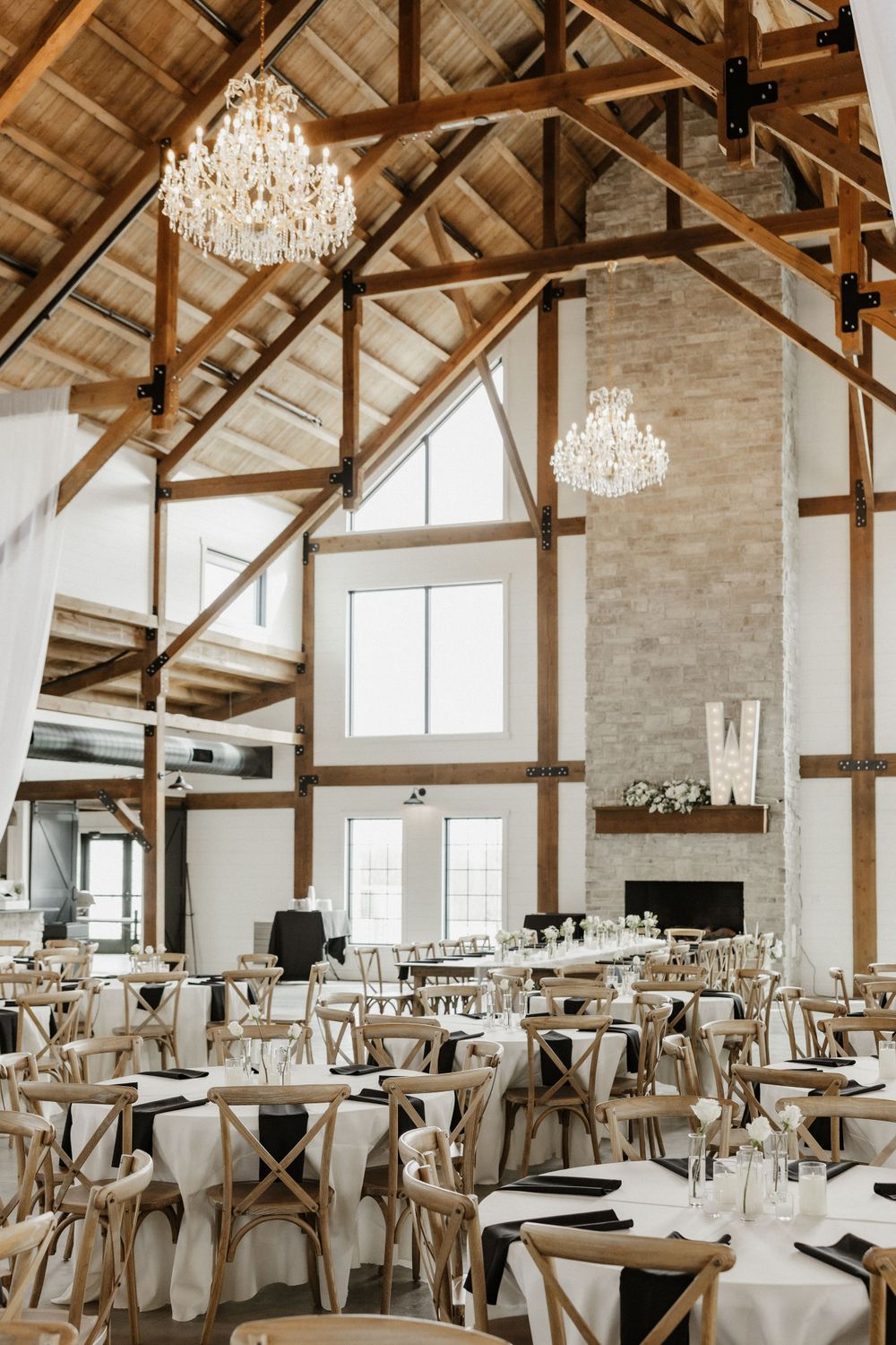 Elegant rustic wedding venue with vaulted wooden beam ceiling, crystal chandeliers, and round dining tables.