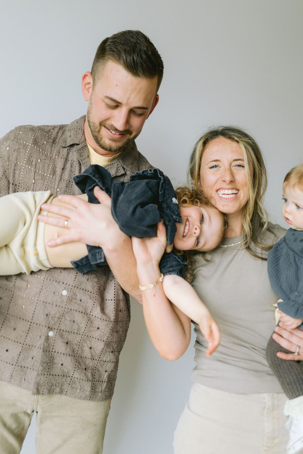 A joyful family portrait shows parents laughing together with their children against a light background.