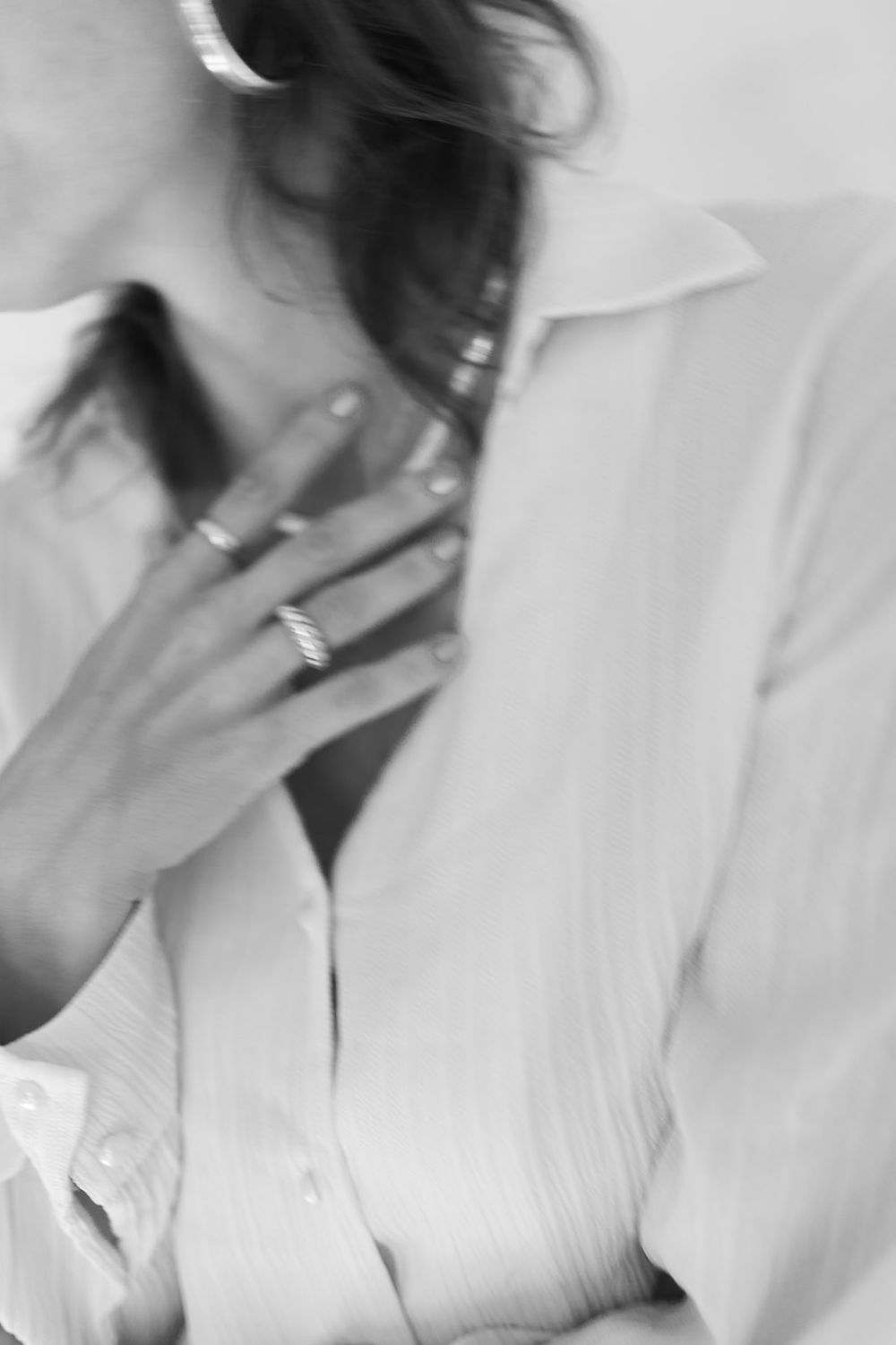 Black and white photo of hands wearing multiple rings against a white button-up shirt in an artistic closeup shot.