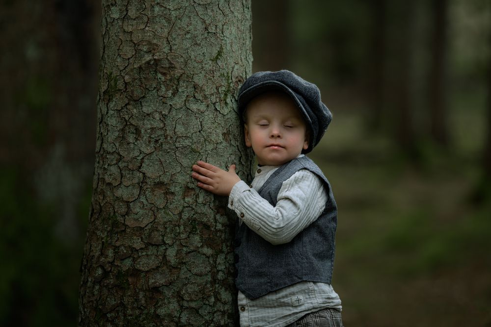 Pojke klädd i gammaldags kläder som upptäcker i skogen. Han kramar ett träd.