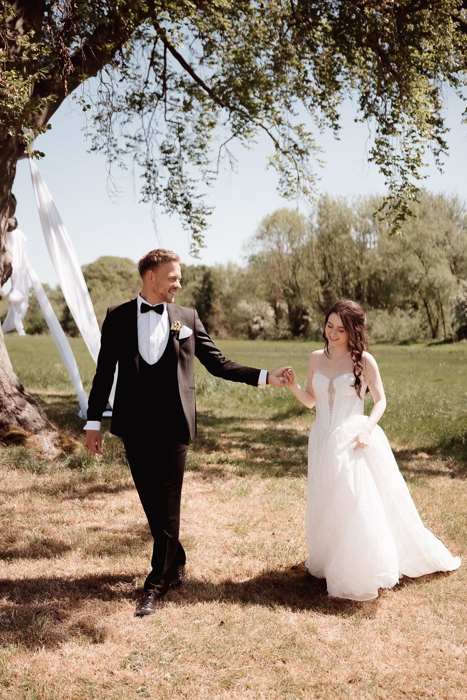 Romantic sunset wedding photo of couple embracing in formal attire with flowing veil.