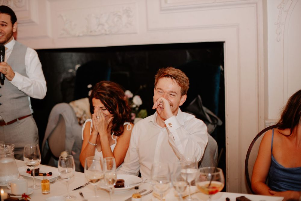 People laughing and having fun during dinner at an elegant reception table with white decor.