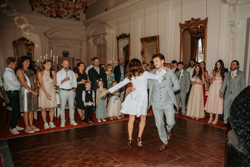 A couple spins together on a dance floor while guests watch during a romantic reception in an ornate ballroom setting.