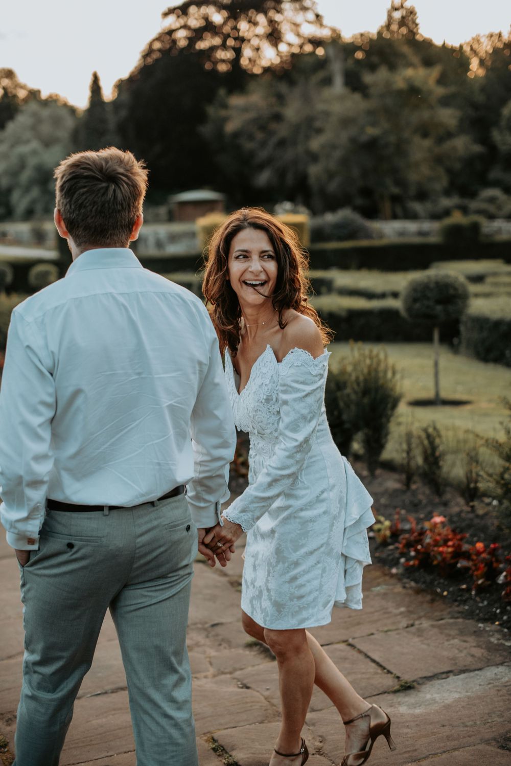 Romantic couple in white outfits dancing together on stone patio at sunset in garden setting.