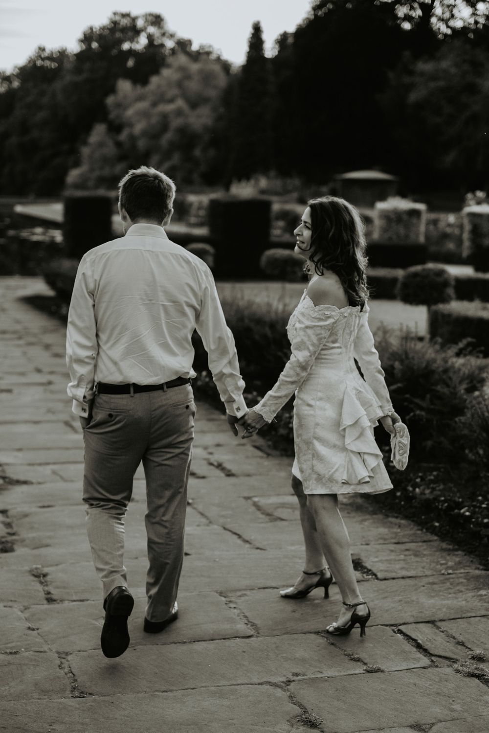 A couple walking together on a stone pathway in black and white, with the woman wearing a white dress.