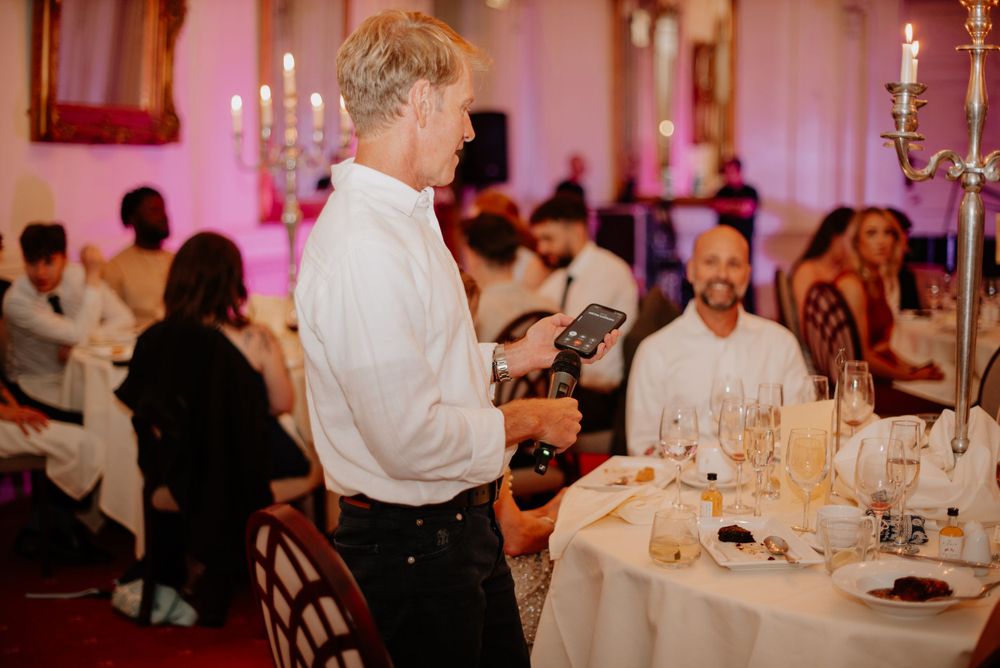 A server looks over a dining table set with candles and wine glasses at a formal restaurant event with pink ambient lighting.