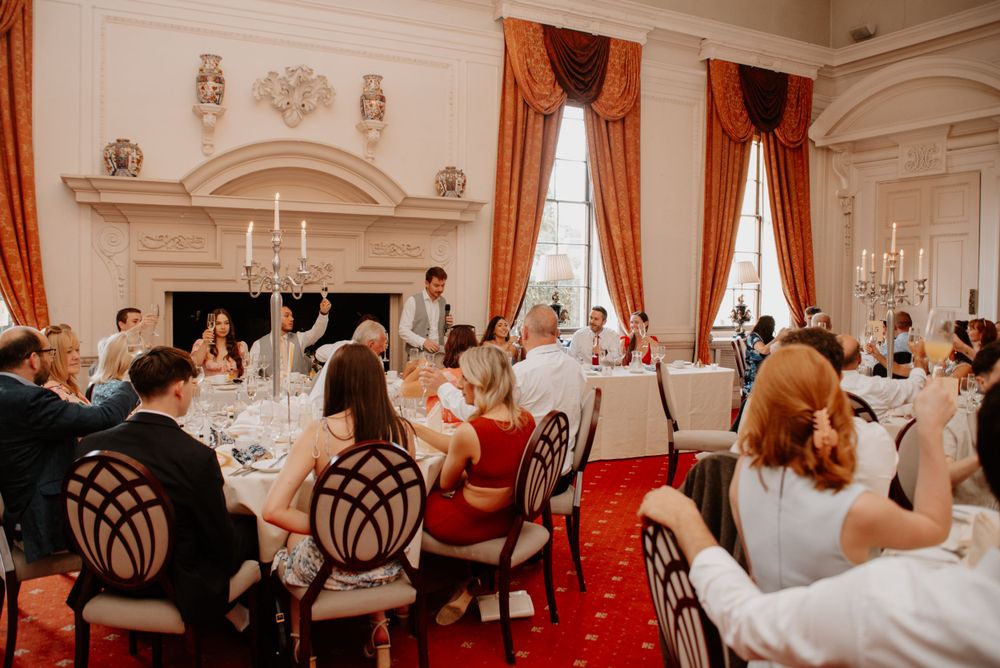Elegant dining room with red carpet and drapes features guests seated at round tables for a formal event.
