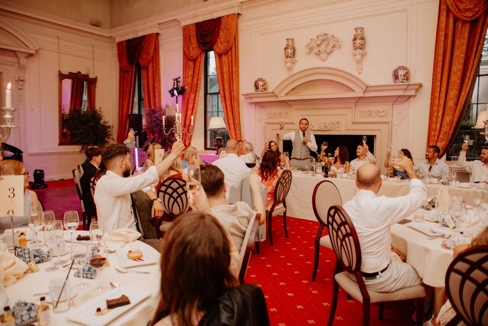 Guests dine in an elegant reception hall with red carpet, ornate fireplace, and classic decor during a formal event.