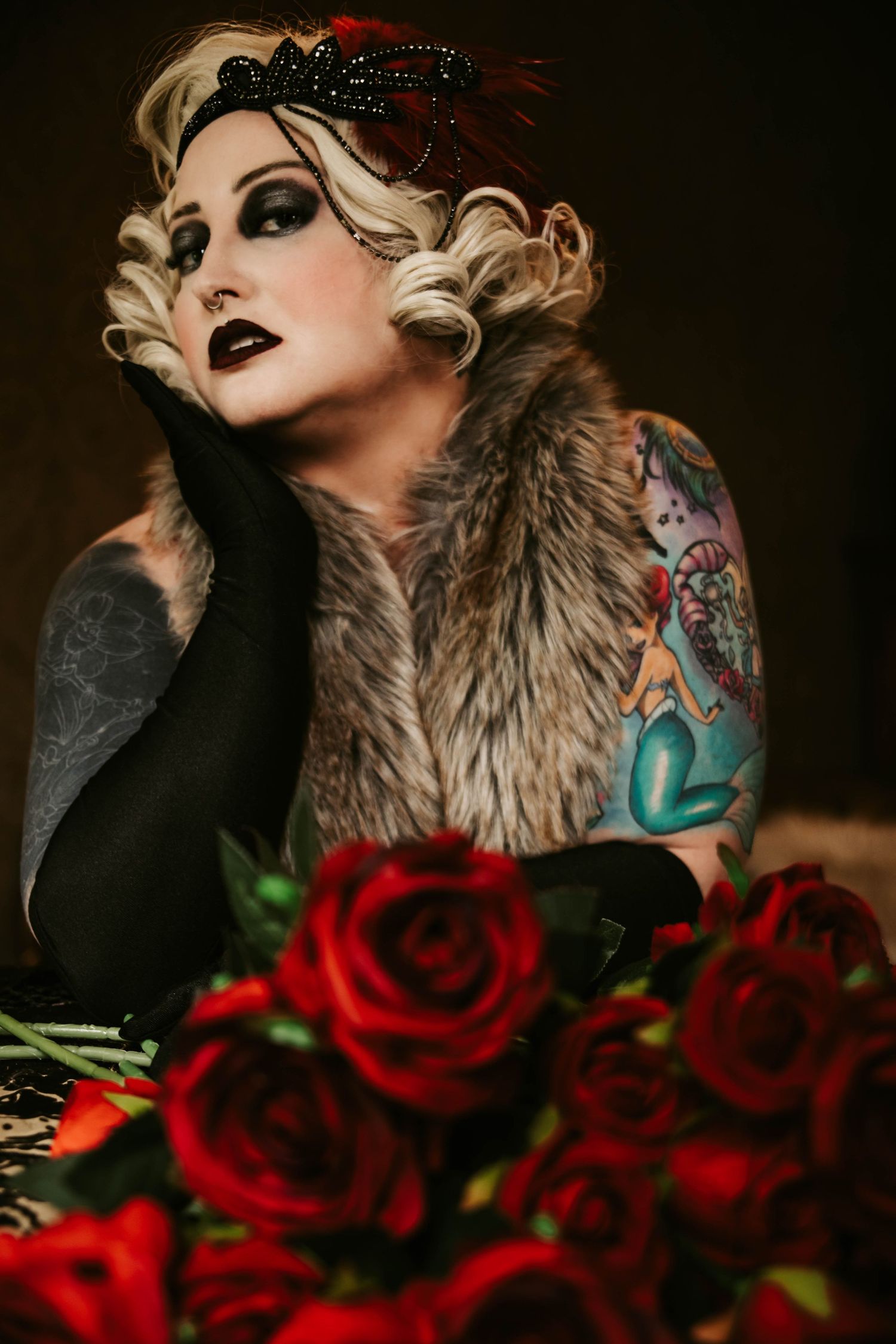 Vintage glamour style photo with fur stole, red roses, dark makeup and 1920s inspired headpiece with visible tattoo art.