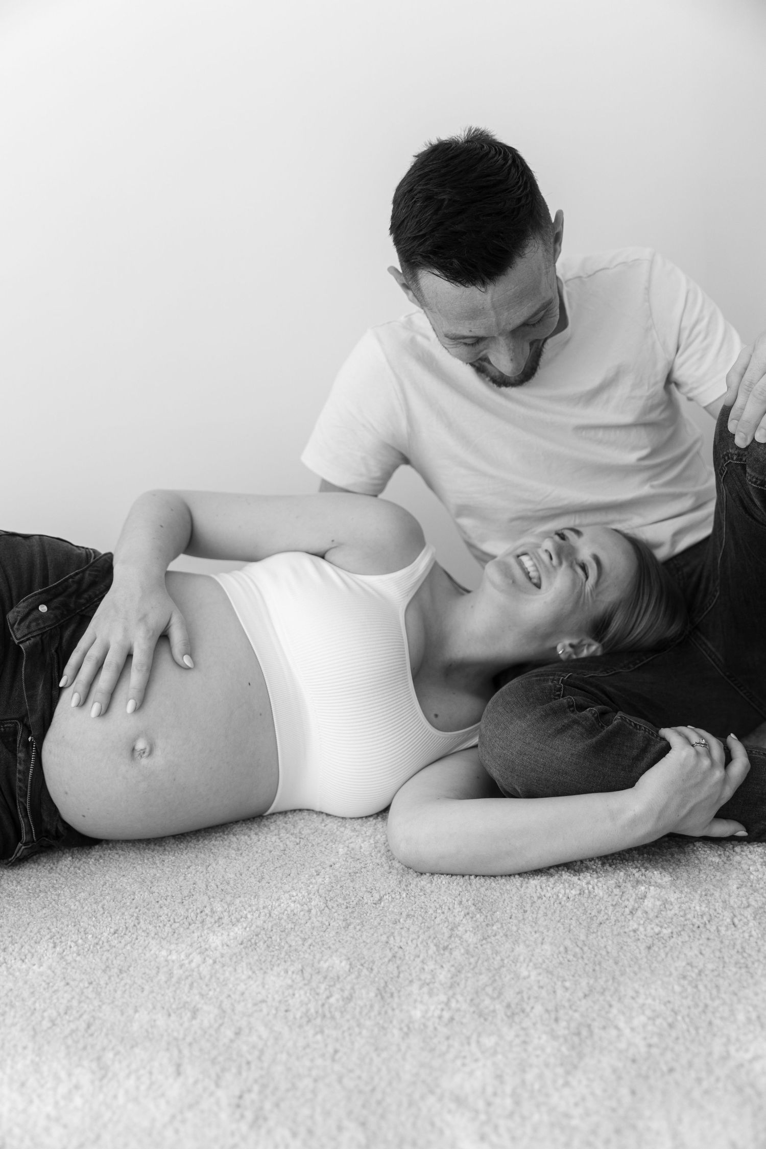 Black and white photo of a couple lying on carpet sharing an intimate moment during pregnancy maternity photoshoot.