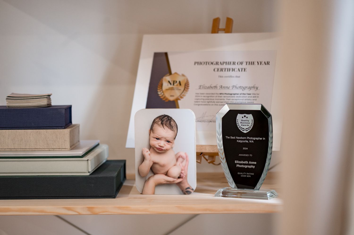 Award plaques and books arranged on a desk with a baby photo frame displayed between them.