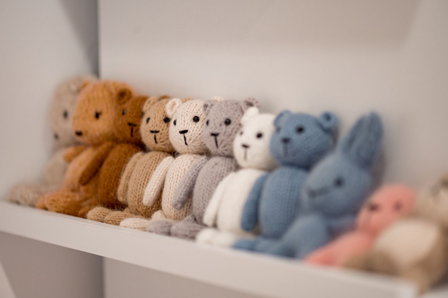 A row of plush teddy bears in gradient colors from brown to blue displayed on a white shelf.
